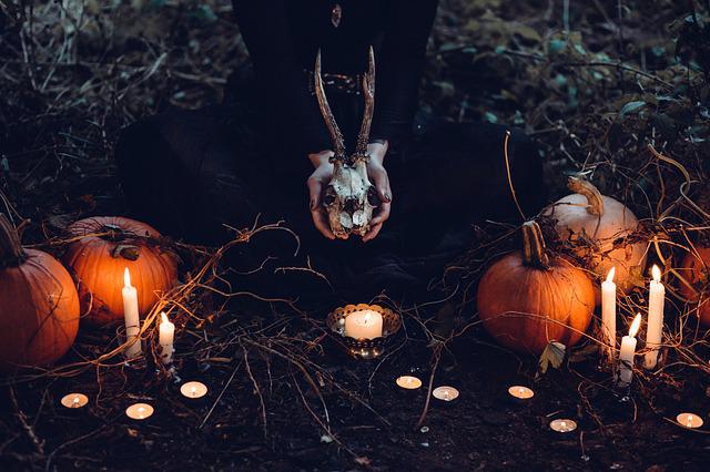 witchy altar with candles, pumpkins and hands holding a skull