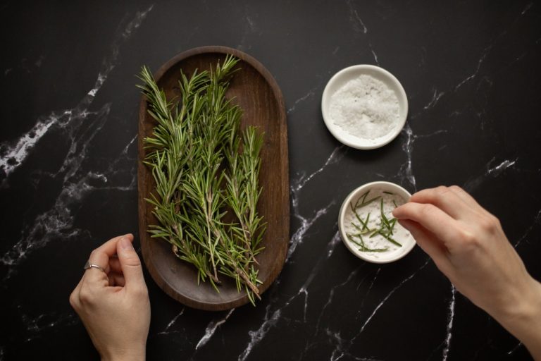 person adding rosemary to a dish