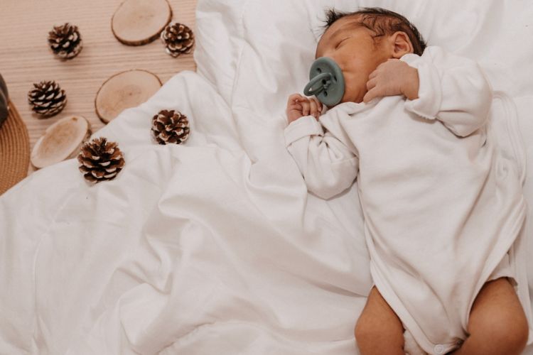 baby on a white sheet with pinecones and apple slices