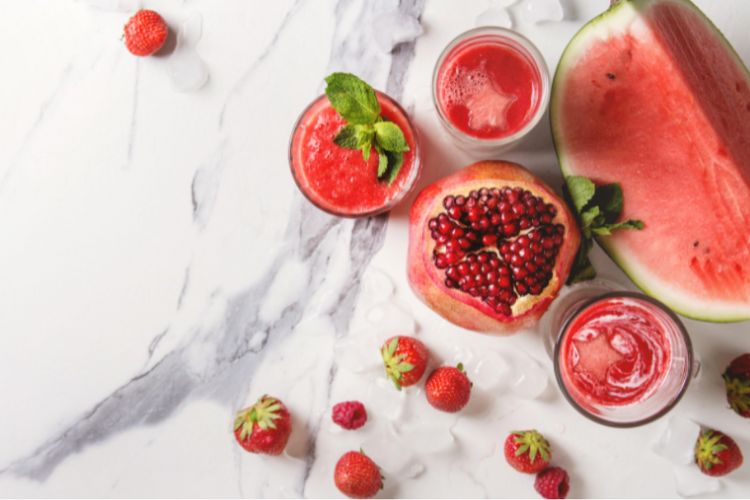 watermelon, strawberries, and pomegranate on a white marble countertop