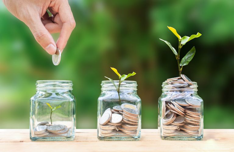 hand adding a coin to an almost empty jar with two other jars that have coins and plants growing