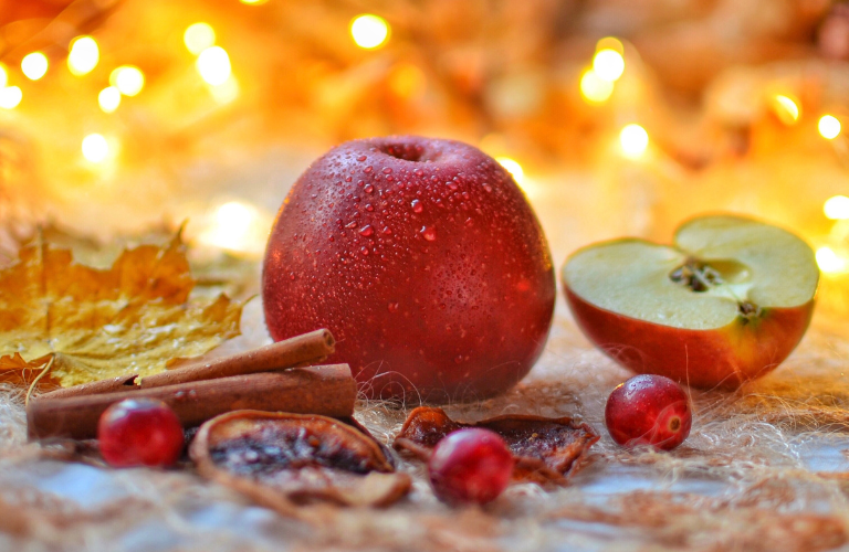 apples, cranberries, cinnamon sticks, dried orange sliced with orange twinkle lights behind