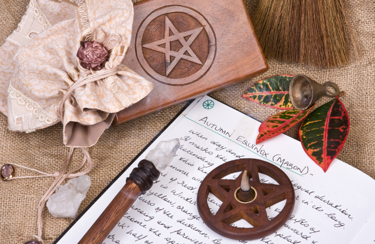 altar table set up with book of shadows that has autumn equinox writing, a crystal tipped wand, and pentagram incense burner